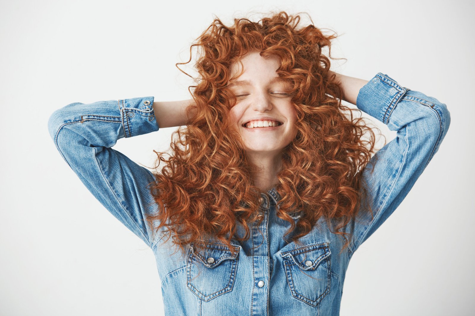Portrait of young foxy beautiful girl touching hair smiling with closed eyes over white baackground.