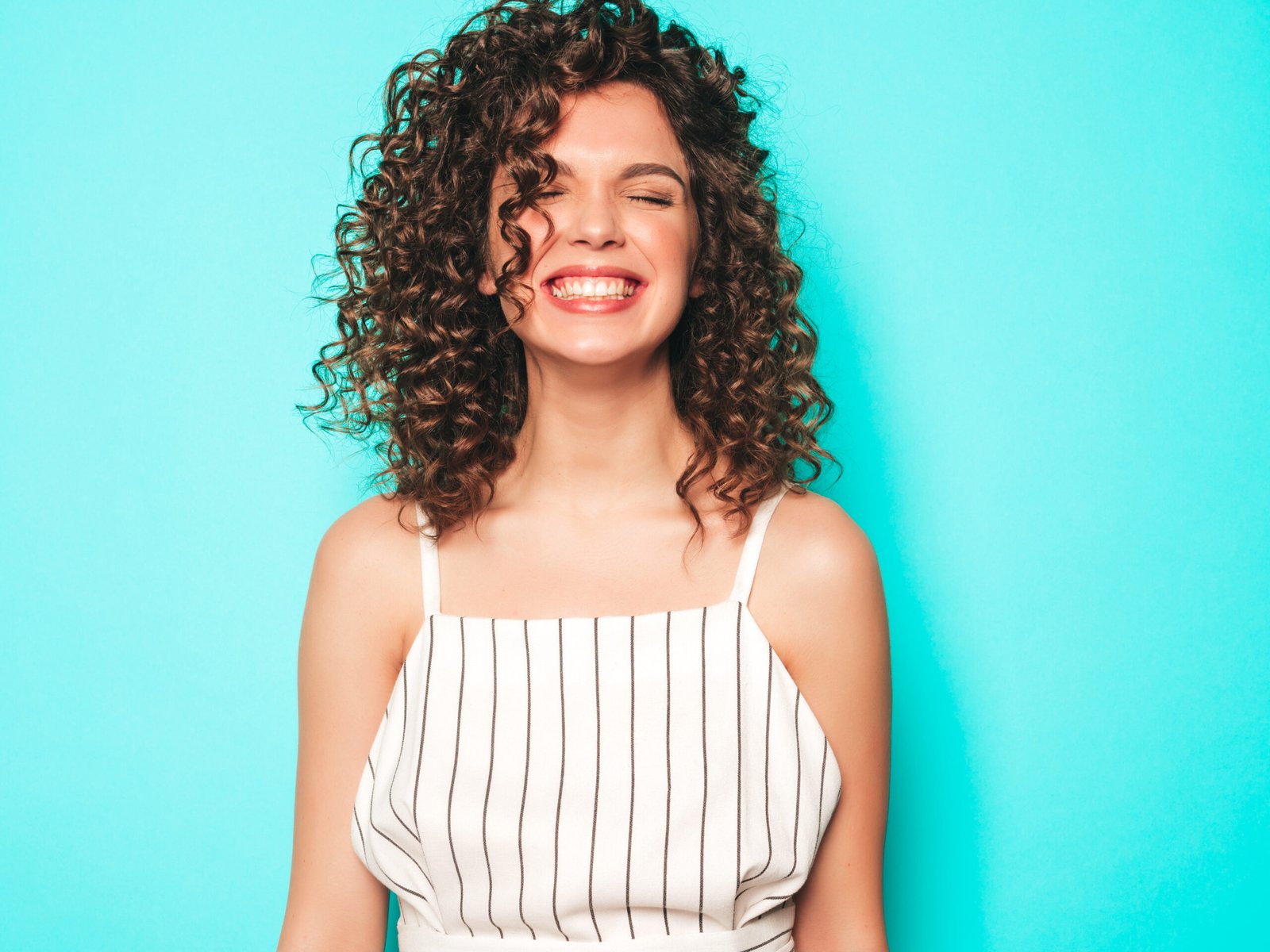 Portrait of beautiful smiling model with afro curls hairstyle dressed in summer hipster clothes.Sexy carefree girl posing in studio near blue wall.Trendy funny and positive woman
