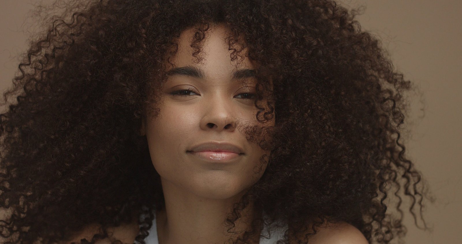 mixed race black woman portrait with big afro hair, curly hair in beige background smiling and laughing closeup
