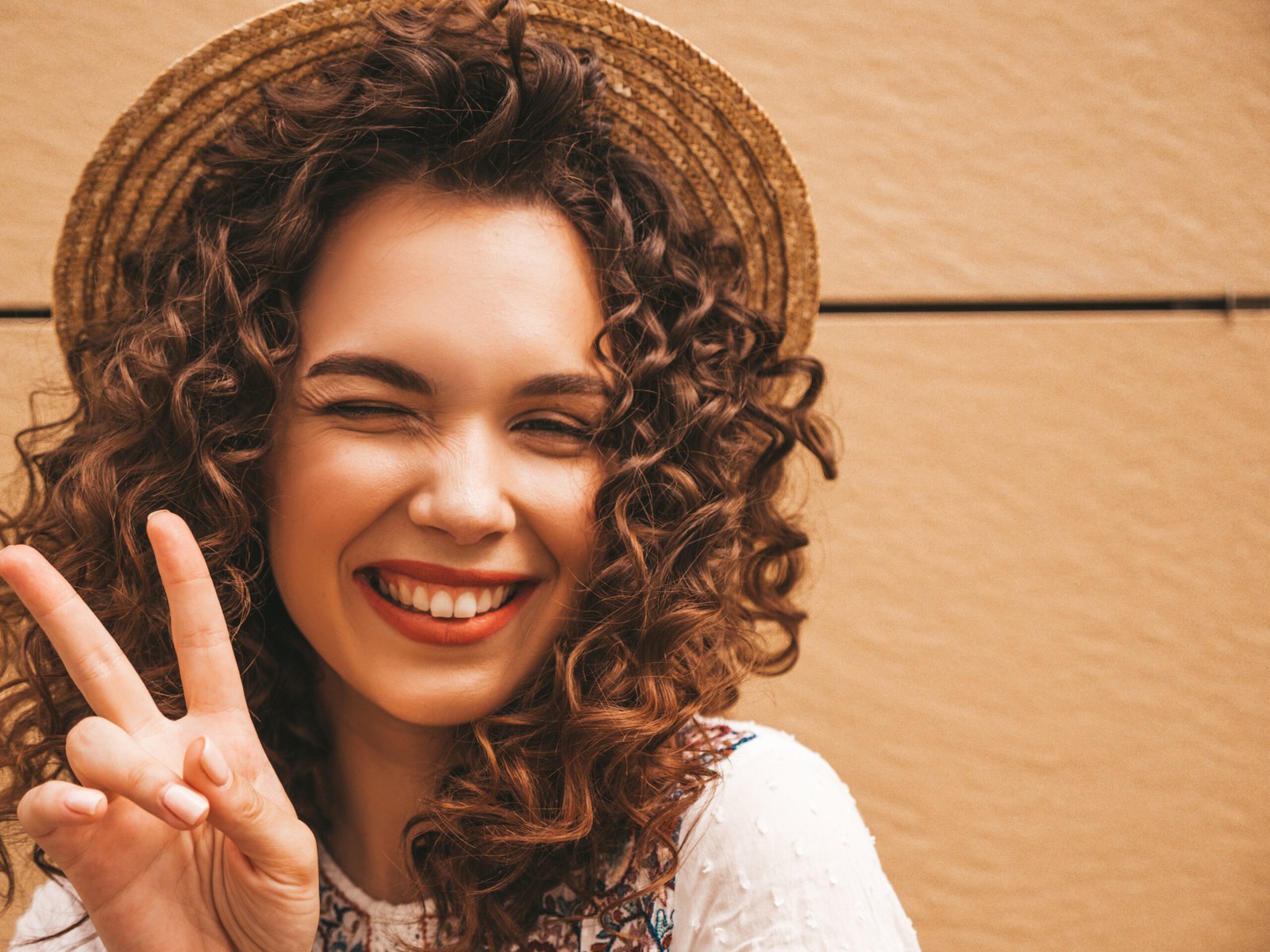 Beautiful smiling model with afro curls hairstyle dressed in summer hipster white dress.Sexy carefree girl posing in the street near yellow wall in hat.Funny and positive woman having fun