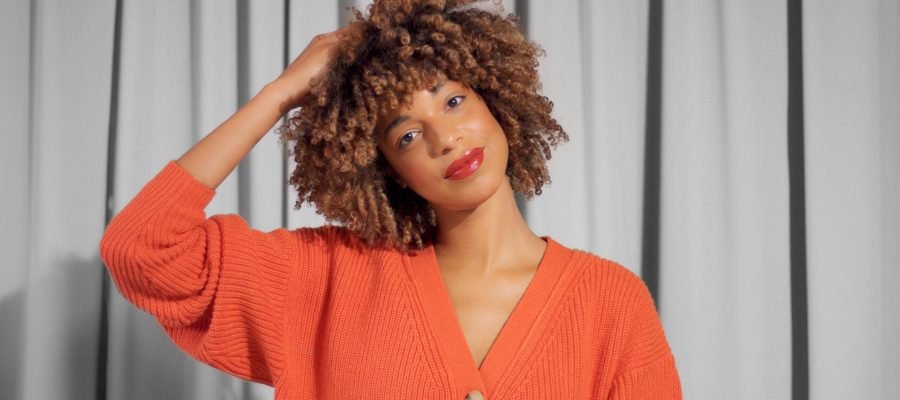 Closeup portrait of mixed race black woman with textured curly afro hair in bright orange jacket with natural makeup for dark skin tones