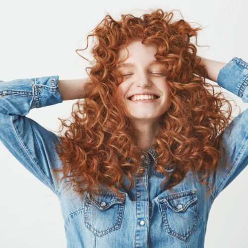 Portrait of young foxy beautiful girl touching hair smiling with closed eyes over white baackground.