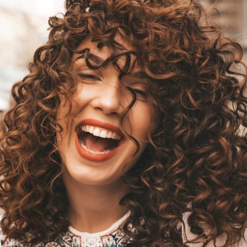 Portrait of beautiful smiling model with afro curls hairstyle.Sexy carefree girl posing in the street background.Trendy  and funny woman shows positive emotions