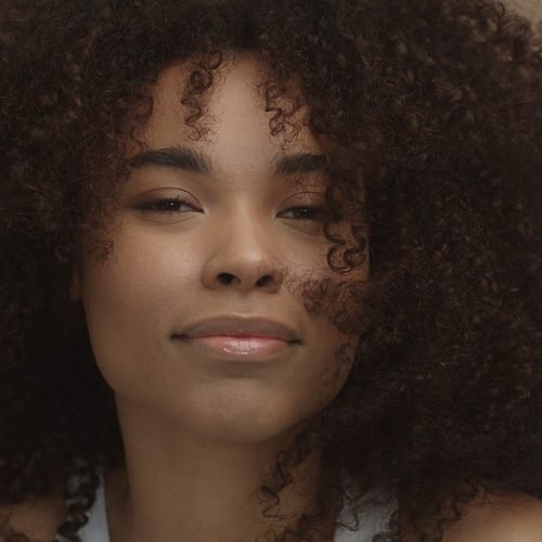 mixed race black woman portrait with big afro hair, curly hair in beige background smiling and laughing closeup